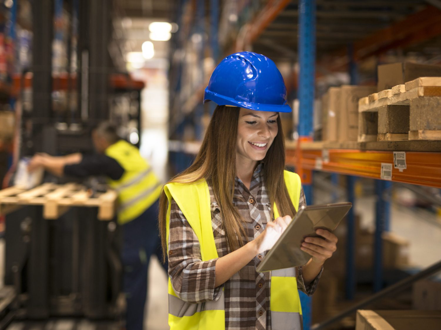 Female warehouse worker holding tablet checking inventory in distribution warehouse.
